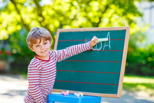 Маленький мальчик за школьной доской практикует буквы — стоковое фото
