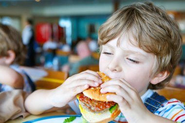 Sevimli sağlıklı okul öncesi çocuk Okul kantininde oturan hamburger yiyor