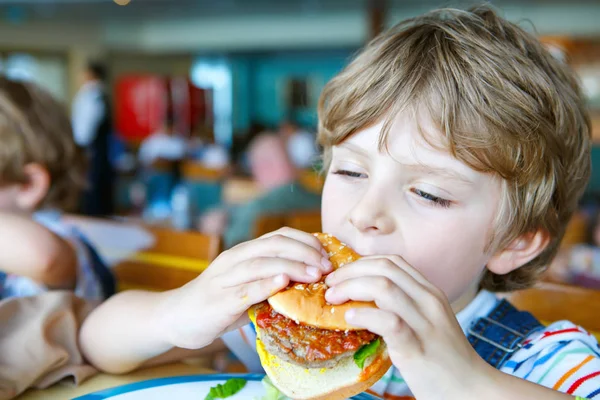 Sevimli sağlıklı okul öncesi çocuk Okul kantininde oturan hamburger yiyor