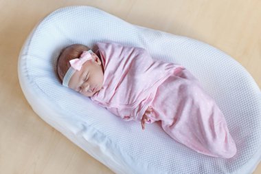 One week old newborn baby girl sleeping wrapped in blanket clipart