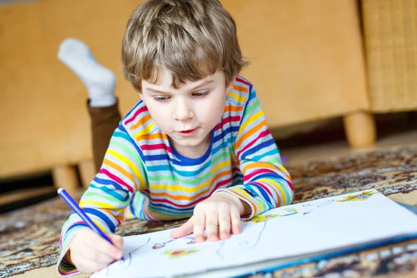 Menino pré-escolar em casa fazendo lição de casa, pintando uma história com canetas coloridas — Fotografia de Stock