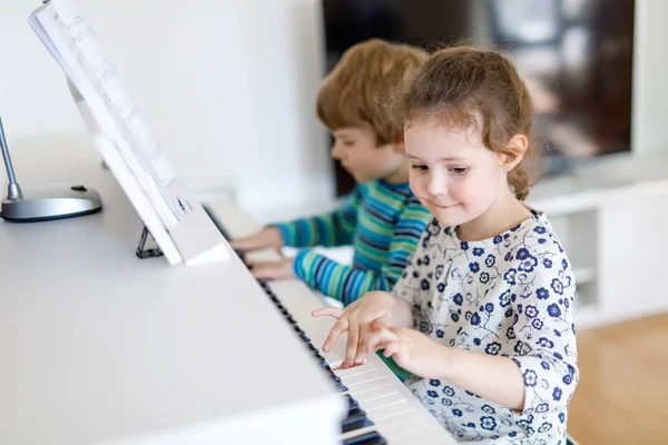 Twee kleine kinderen meisje en jongen speelde piano in de woonkamer of muziekschool — Stockfoto