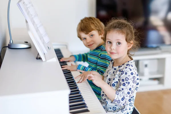 Две маленькие девочки и мальчик играют на фортепиано в гостиной или музыкальной школе — стоковое фото