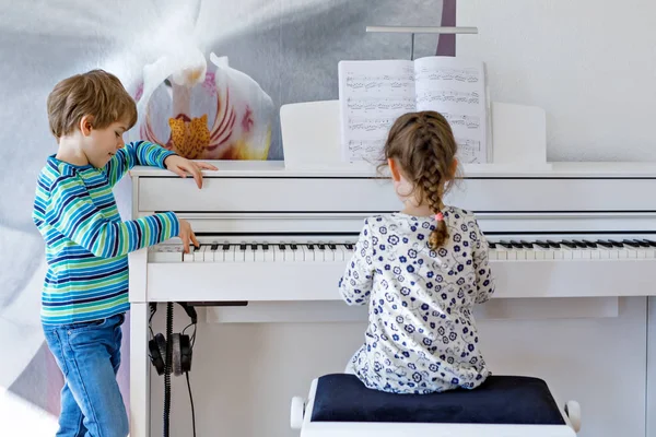 Dos niños pequeños niña y niño tocando el piano en la sala de estar o la escuela de música — Foto de Stock