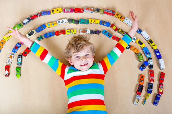 Cute little blond kid boy playing with lots of toy cars indoor. — Stock Photo, Image