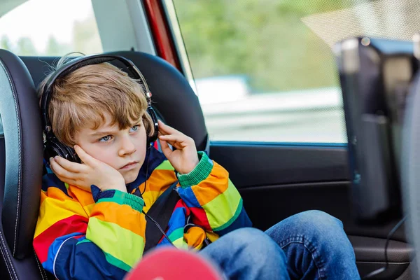 Little blond kid boy watching tv or dvd with headphones during long car drive — Stock Photo, Image