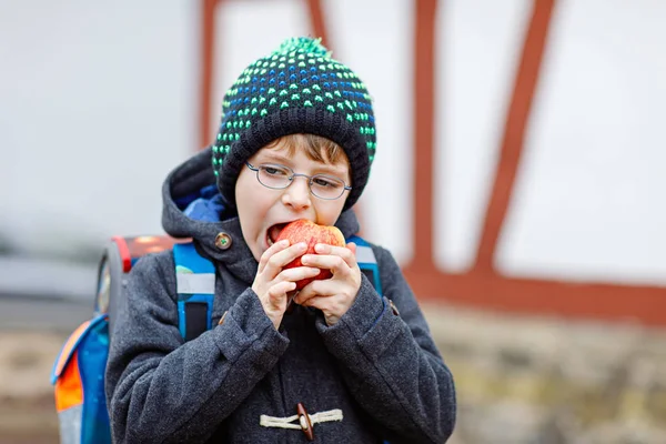 Маленький мальчик в очках идет из школы и ест яблоко — стоковое фото