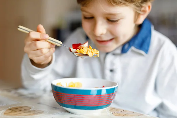 Kleiner blonder Schuljunge isst Müsli mit Milch und Beeren, frische Erdbeeren zum Frühstück — Stockfoto