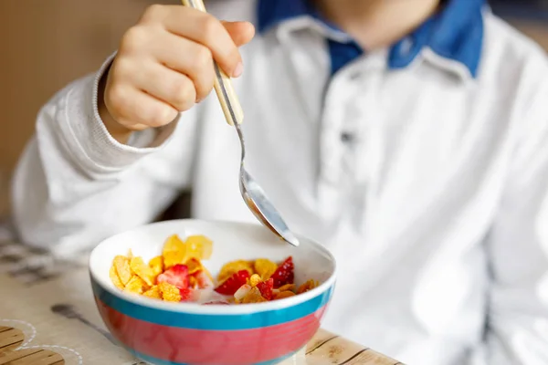Niño de escuela rubio comiendo cereales con leche y bayas, fresa fresca para el desayuno —  Fotos de Stock