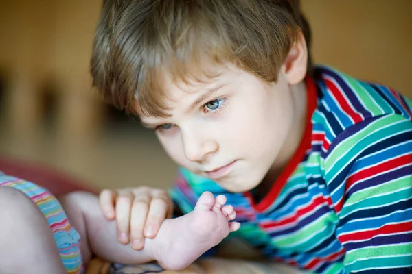 Malý kluk kluk líbat a hrát si s nohou novorozeně. — Stock fotografie