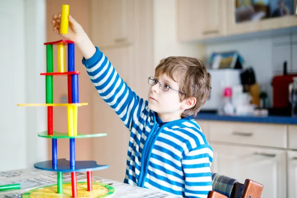 Мальчик в очках играет с большим количеством красочных деревянных блоков игры в помещении — стоковое фото