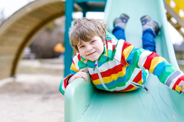 Menino garoto loiro feliz se divertindo e deslizando no parque infantil ao ar livre — Fotografia de Stock