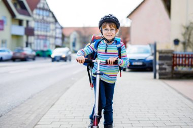 Kasklı küçük çocuk şehirde scooterıyla geziyor.
