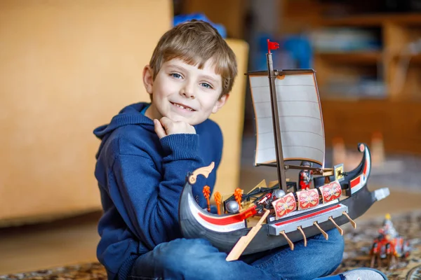 Маленький блондин дошкольник, играющий с игрушечным кораблем в помещении — стоковое фото