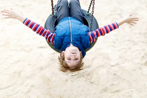 Engraçado garoto menino se divertindo com corrente swing no playground ao ar livre — Fotografia de Stock