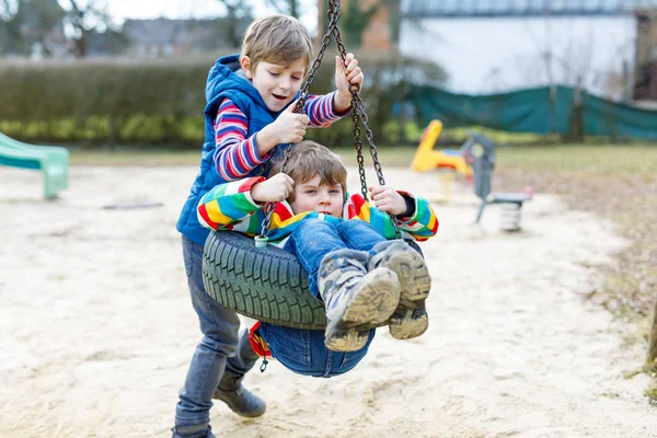 Dos niños pequeños que se divierten con el oscilación de la cadena en el patio al aire libre — Foto de Stock