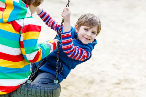 Two little kid boys having fun with chain swing on outdoor playground — Stock Photo, Image