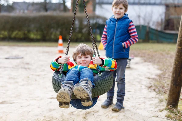 Dos niños pequeños que se divierten con el oscilación de la cadena en el patio al aire libre — Foto de Stock