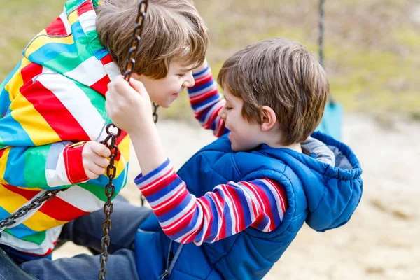 Dos niños pequeños que se divierten con el oscilación de la cadena en el patio al aire libre —  Fotos de Stock
