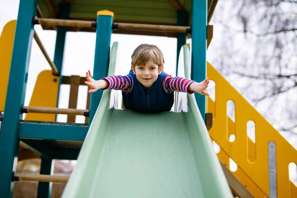 Happy blond kid boy having fun and sliding on outdoor playground — Stock Photo, Image