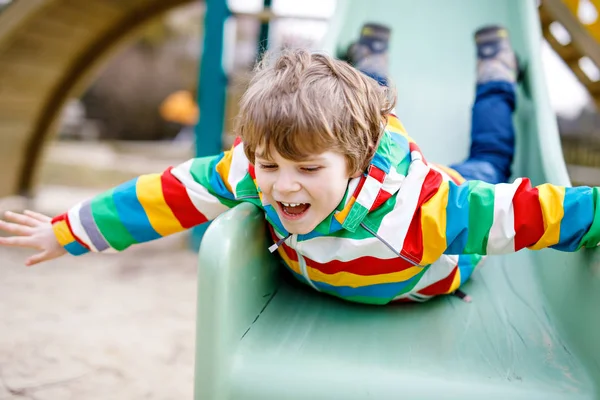 Happy blond kid boy having fun and sliding on outdoor playground — Stock Photo, Image