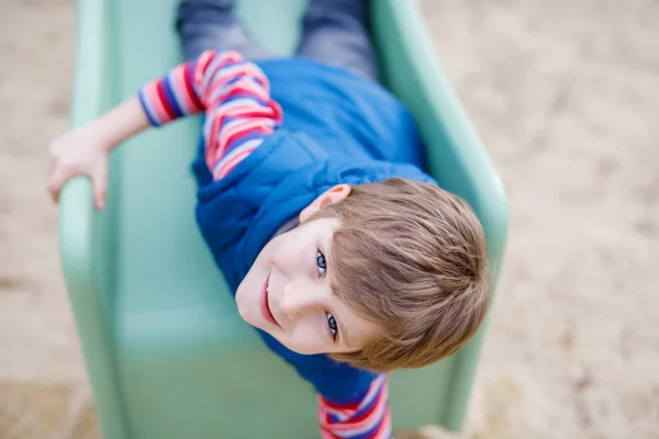 Niño rubio feliz divirtiéndose y deslizándose en el patio al aire libre — Foto de Stock