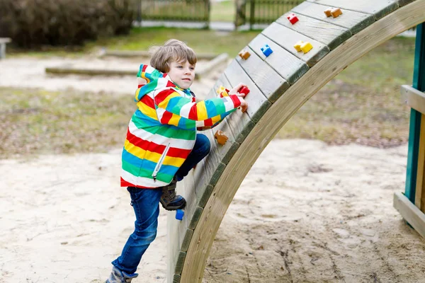 Gelukkig blond kind jongen met plezier en klimmen op de speelplaats — Stockfoto