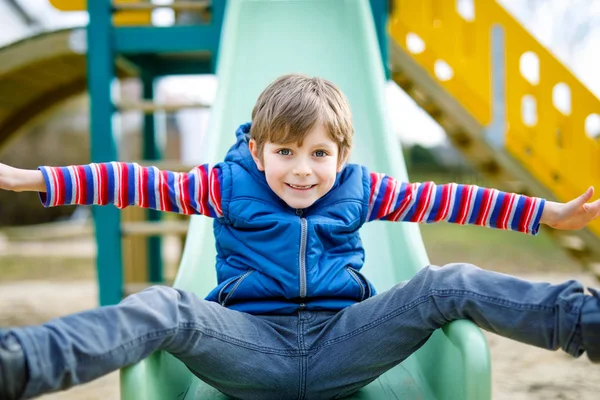 Glada blond kid boy roar och glidande på lekplatsen utomhus — Stockfoto