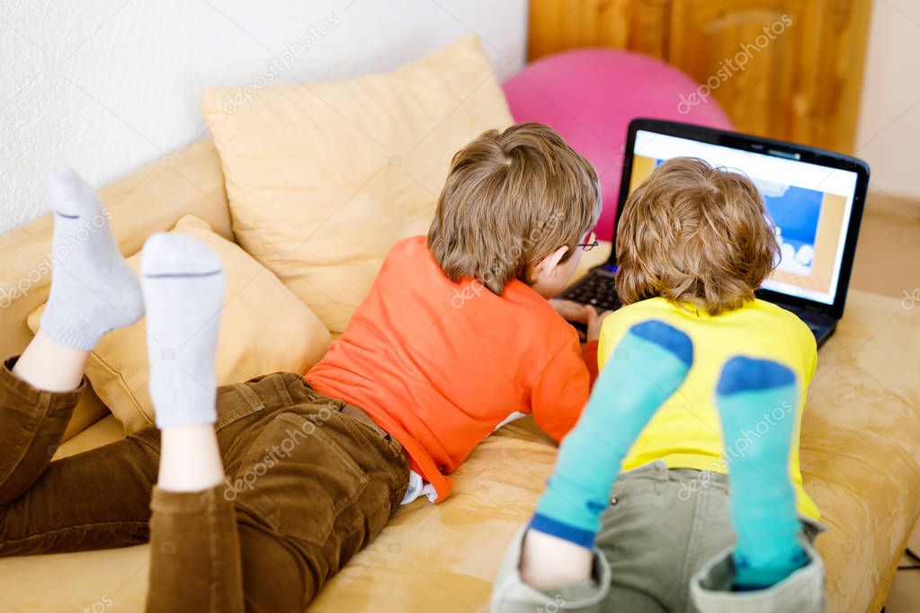 Happy little brothers, adorable kid boys watching television while lying