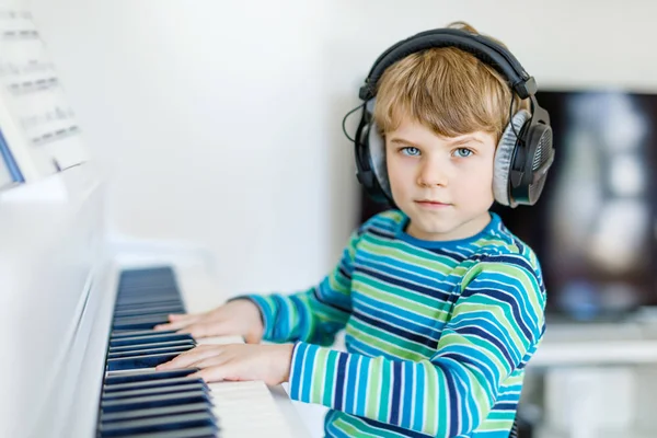 Beautiful little kid boy playing piano in living room or music school — Stock Photo, Image