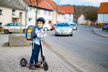 Kasklı küçük çocuk şehirde scooterıyla geziyor.