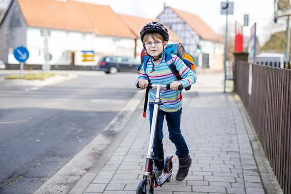 Petit garçon en casque chevauchant avec son scooter dans la ville — Photo