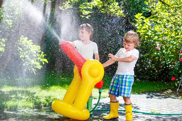 Два маленьких мальчика играют в разбрызгиватель воды из садового шланга — стоковое фото