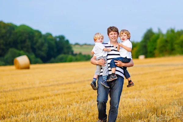 Father holding two children on arms on wheat field in summer — Stock Photo, Image