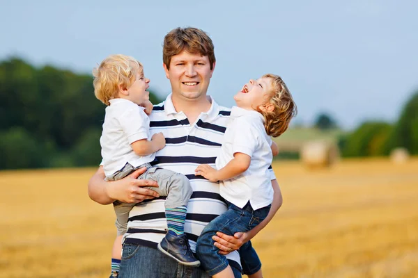 Father holding two children on arms on wheat field in summer — Stock Photo, Image