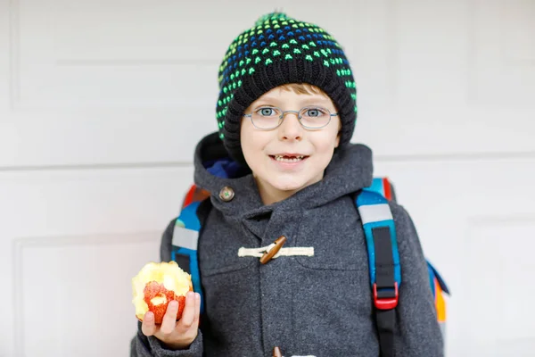Ragazzino con gli occhiali da vista che cammina dalla scuola e mangia mela — Foto Stock
