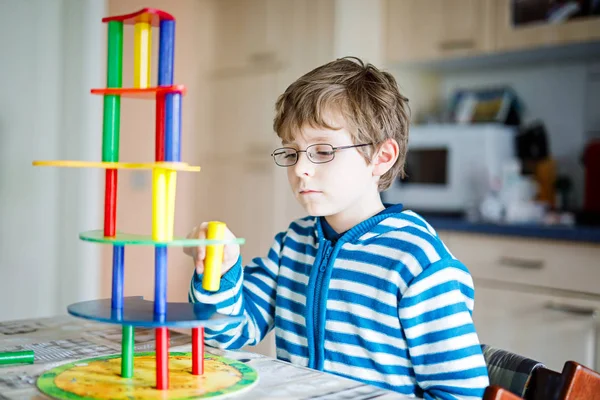 Kid boy with glasses playing with lots of colorful wooden blocks game indoor