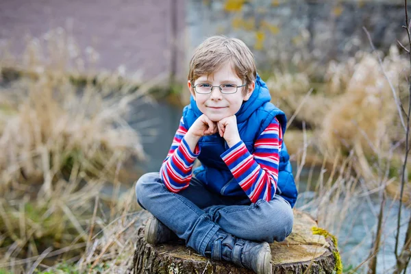 Хлопчик з випадковим барвистим одягом та окулярами, що сидять на пеньках на дереві — стокове фото