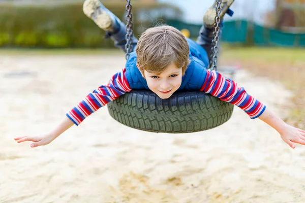 Lustiger Junge hat Spaß mit Kettenschaukel auf Spielplatz — Stockfoto