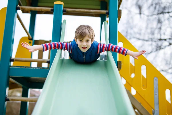 Menino garoto loiro feliz se divertindo e deslizando no parque infantil ao ar livre — Fotografia de Stock