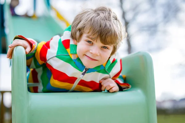 Glada blond kid boy roar och glidande på lekplatsen utomhus — Stockfoto