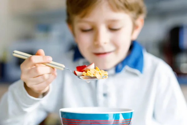 Kleiner blonder Schuljunge isst Müsli mit Milch und Beeren, frische Erdbeeren zum Frühstück — Stockfoto