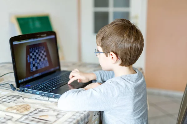 Мальчик в очках играет в шахматы онлайн на компьютере — стоковое фото