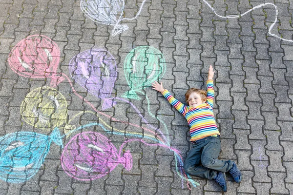 Мальчик веселится с разноцветными воздушными шарами, рисуя мелом — стоковое фото