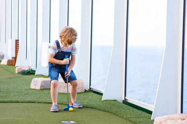 Kleiner Junge spielt Minigolf auf Kreuzfahrtschiff. — Stockfoto