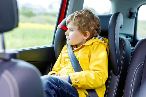 Adorabile carino bambino in età prescolare seduto in auto in cappotto giallo pioggia . — Foto Stock