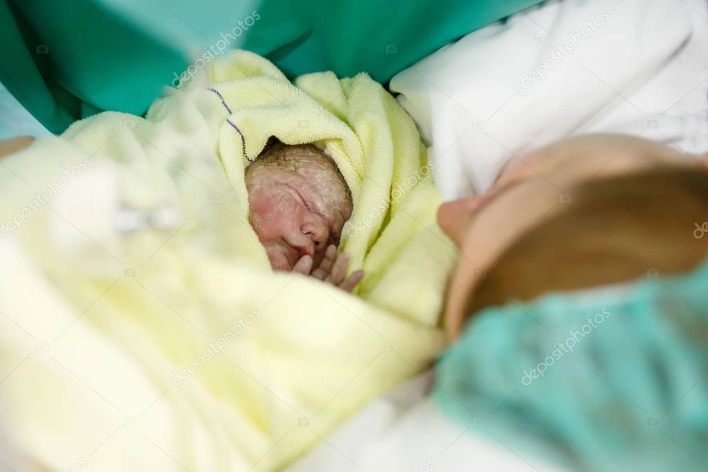 Newborn baby wrapped in blankets after birth. Mother looking for the first time on new born daughter