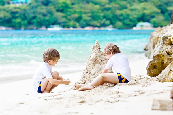 Due bambini ragazzi che costruiscono castello di sabbia sulla spiaggia tropicale — Foto Stock