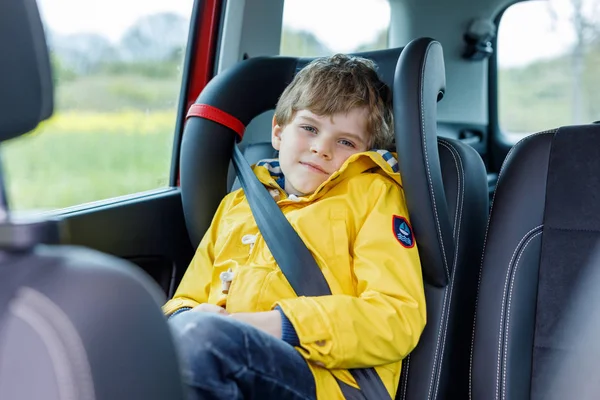 Ładny ładny przedszkolu dziecko chłopiec siedzi w samochodzie w Płaszcz przeciwdeszczowy żółty. — Zdjęcie stockowe