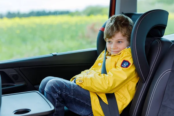 Adorable mignon garçon d'âge préscolaire assis en voiture en imperméable jaune . — Photo